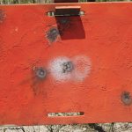 Red metal plate showing bullet splash