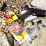 AR-15 on a bed of river rock with two Hipertouch triggers in the packaging