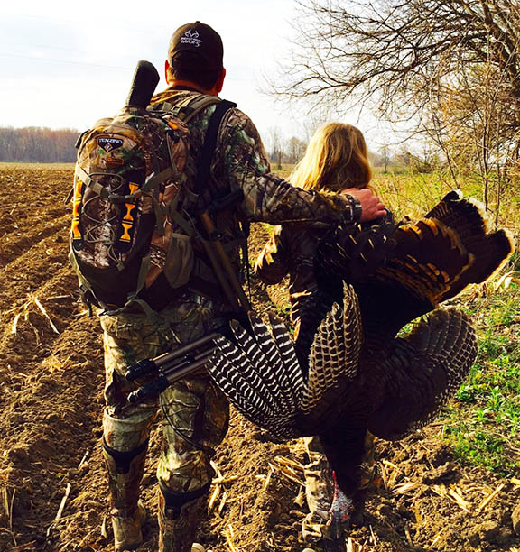 Father standing next to daughter who is holding a wild turkey slung over her back