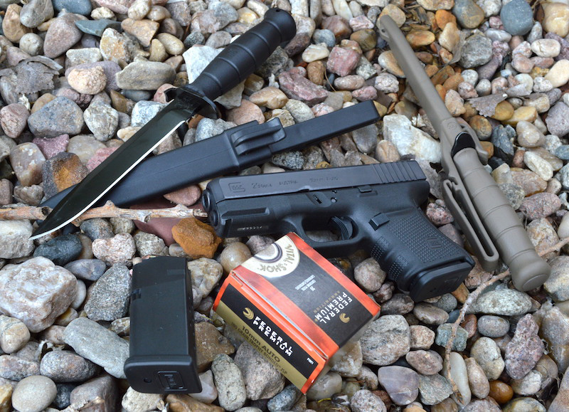 Glock 29 with a spare magazine, knives, and a box of federal Premium ammunition