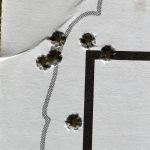 Paper target with bullet holes in the corner of a square