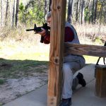 Bob Campbell shooting a rifle from behind a wood post