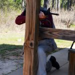 Bob Campbell shooting a rifle from behind a wood post