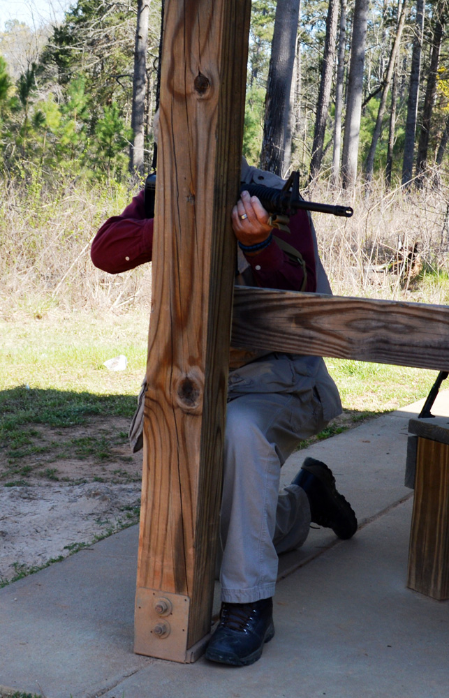 Bob Campbell shooting a rifle from behind a wood post for cover and concealment