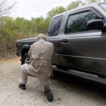 Bob Campbell crouching behind a pickup truck to provide concealment and cover