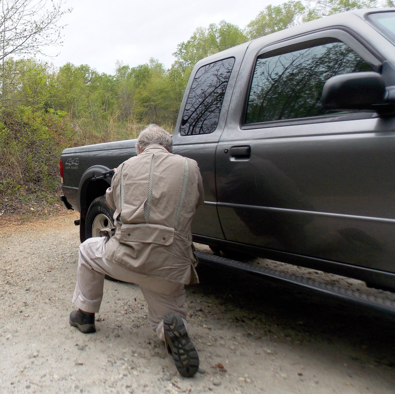 Bob Campbell crouching behind a pickup truck to provide cover and concealment