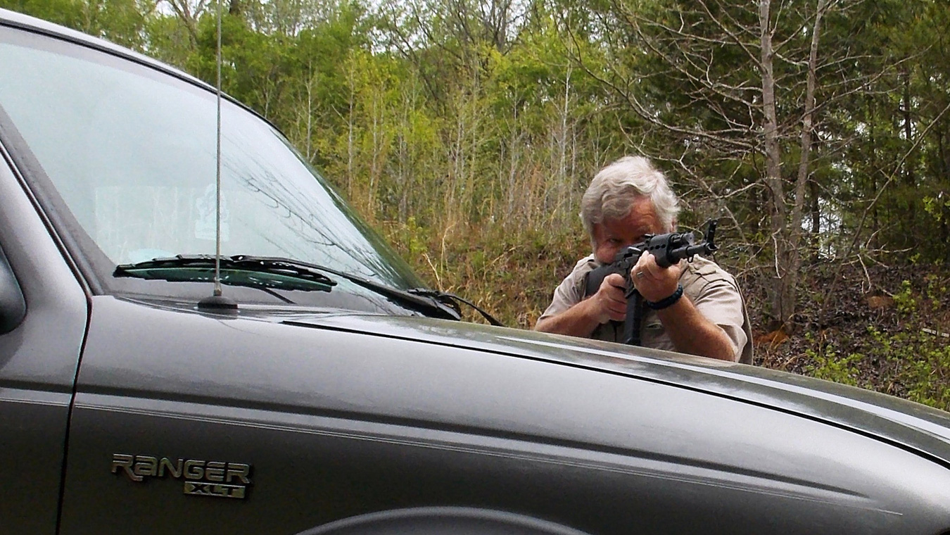 Bob Campbell shooting a rifle over the hood of a pickup truck