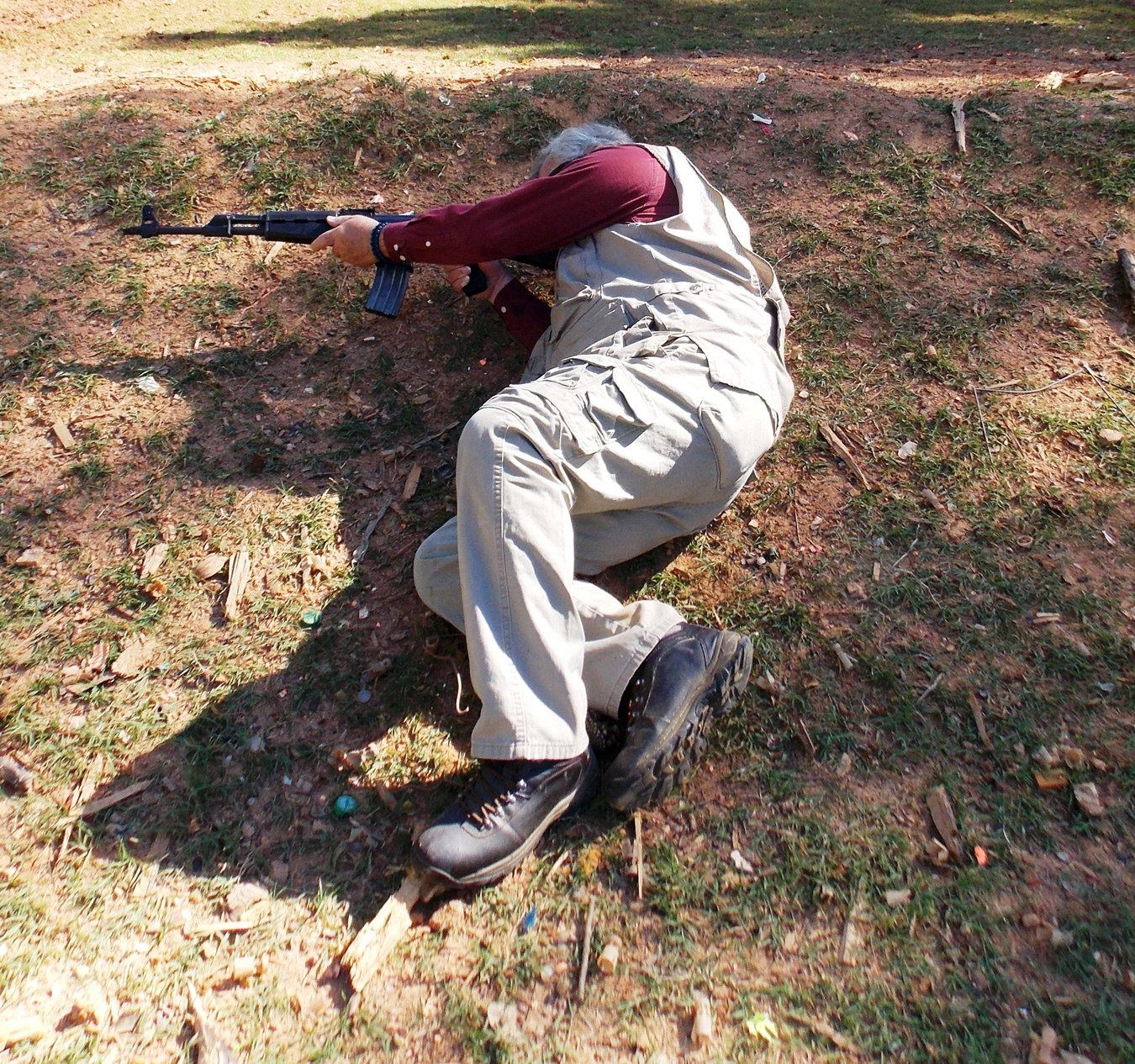 Man firing a rifle while laying on his side using topography for cover