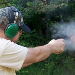 Man with green hearing muffs firing a 1911 pistol