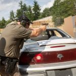 Man training to fire a pistol over the trunk of a car