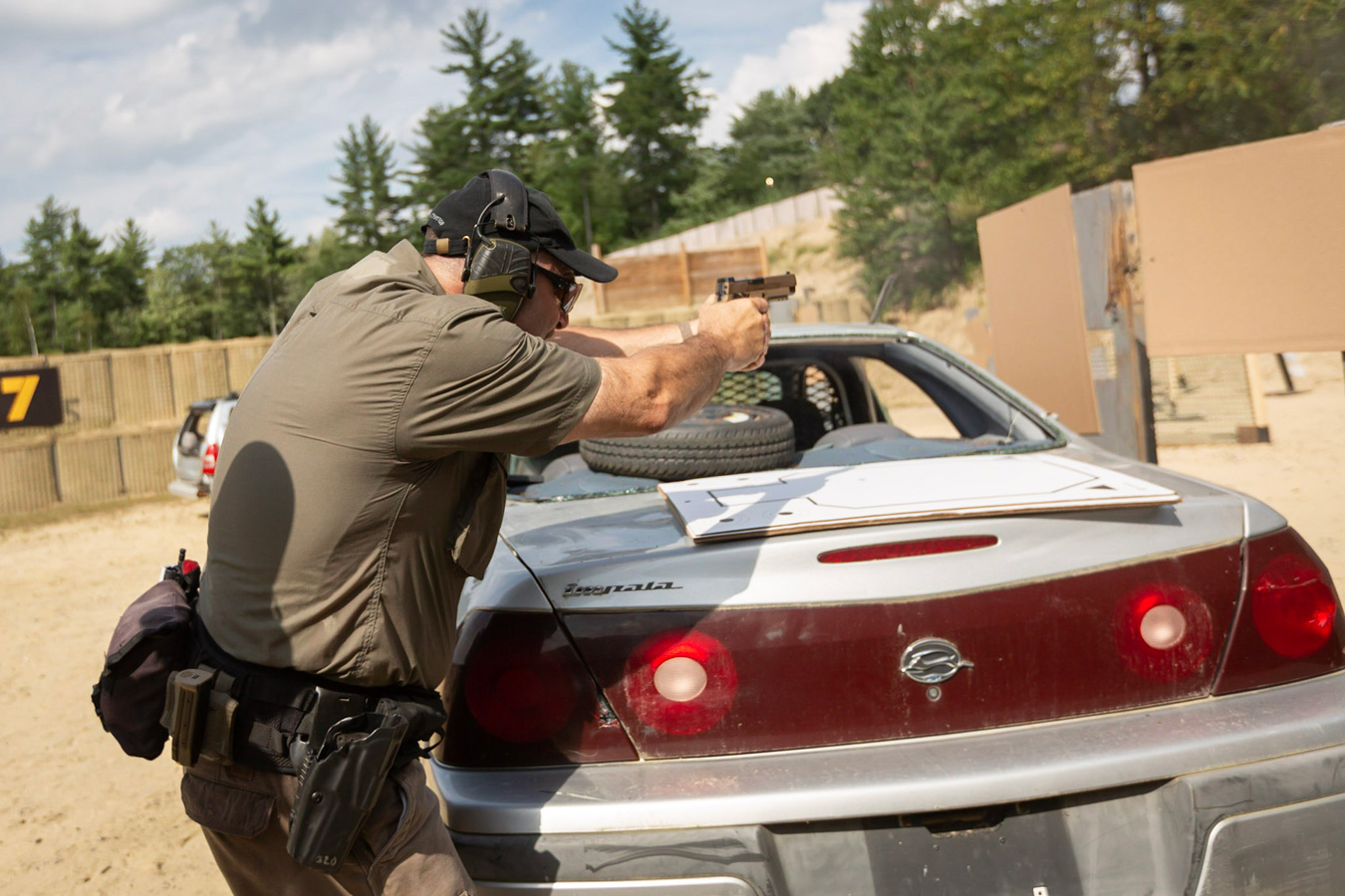 Man training to fire a pistol over the trunk of a car
