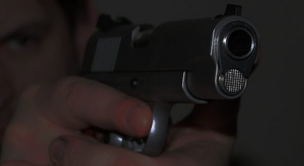 Dark photo of a hand holding a pistol extolling gun control
