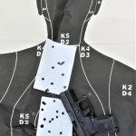 pistol atop a silhouette target with bullet holes