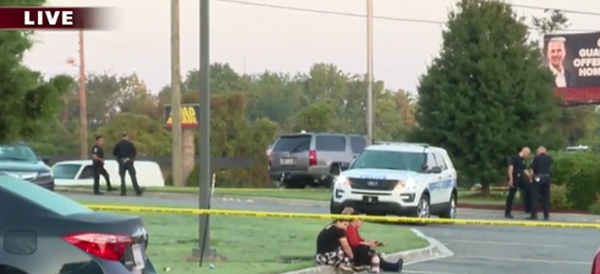 two armed good guys sitting on a curb behind police tape with police cruiser in the background