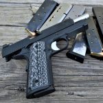 Guncrafter Commander 1911 pistil with slide locked back lying on several loaded magazines
