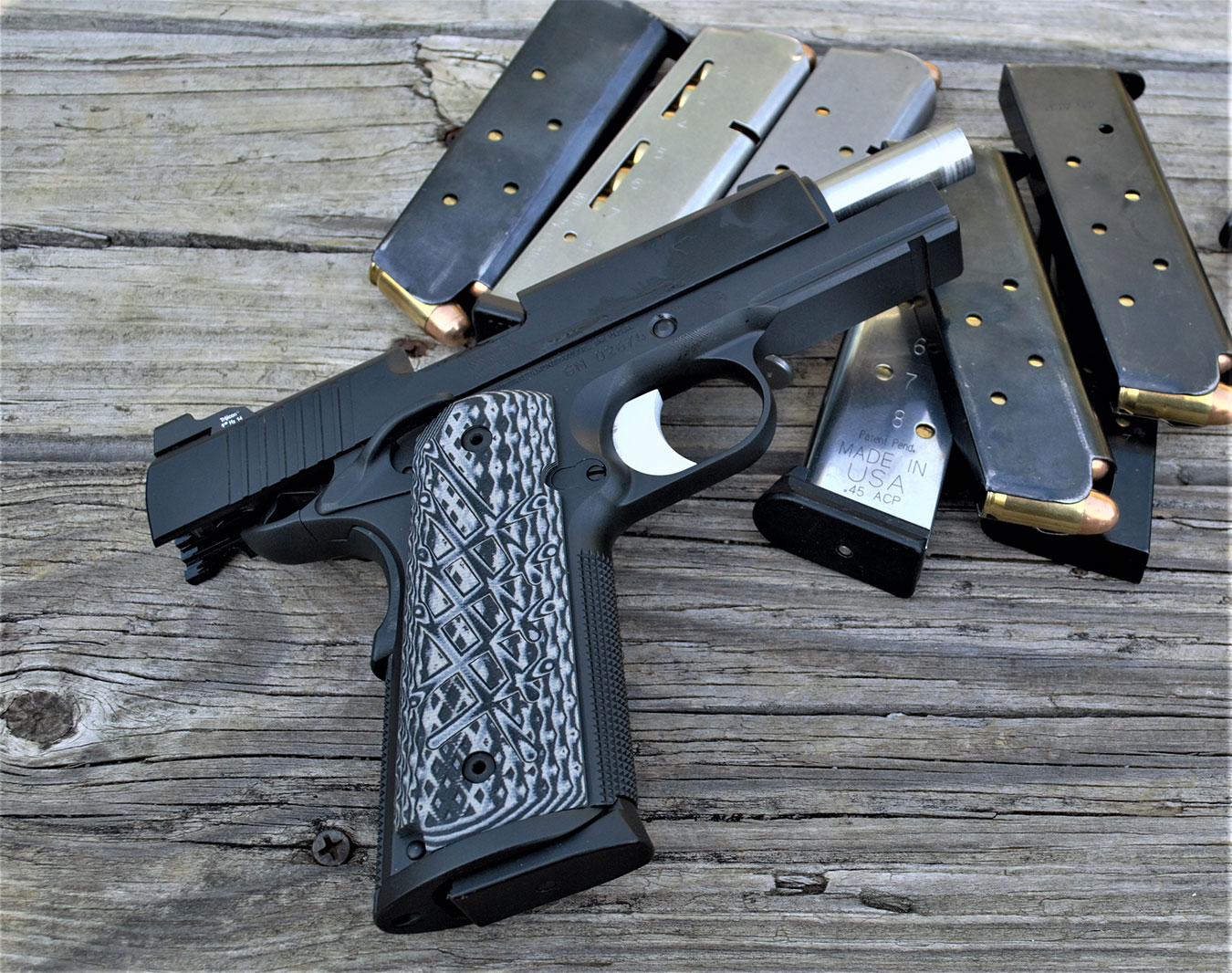 Guncrafter Commander 1911 pistil with slide locked back lying on several loaded magazines