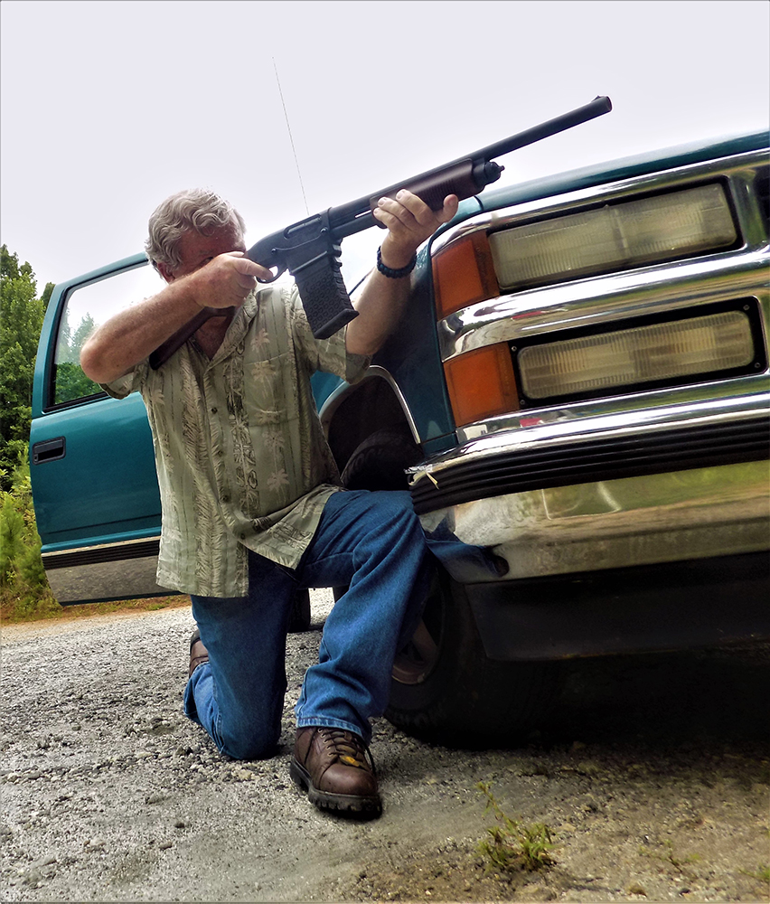 Bob Campbell shooting the Remington 870 DM shotgun while kneeling behind a car
