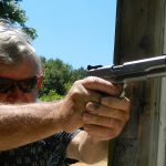 Bob Campbell shooting a 1911 10mm pistol with a two-handed grip braced against a baricade