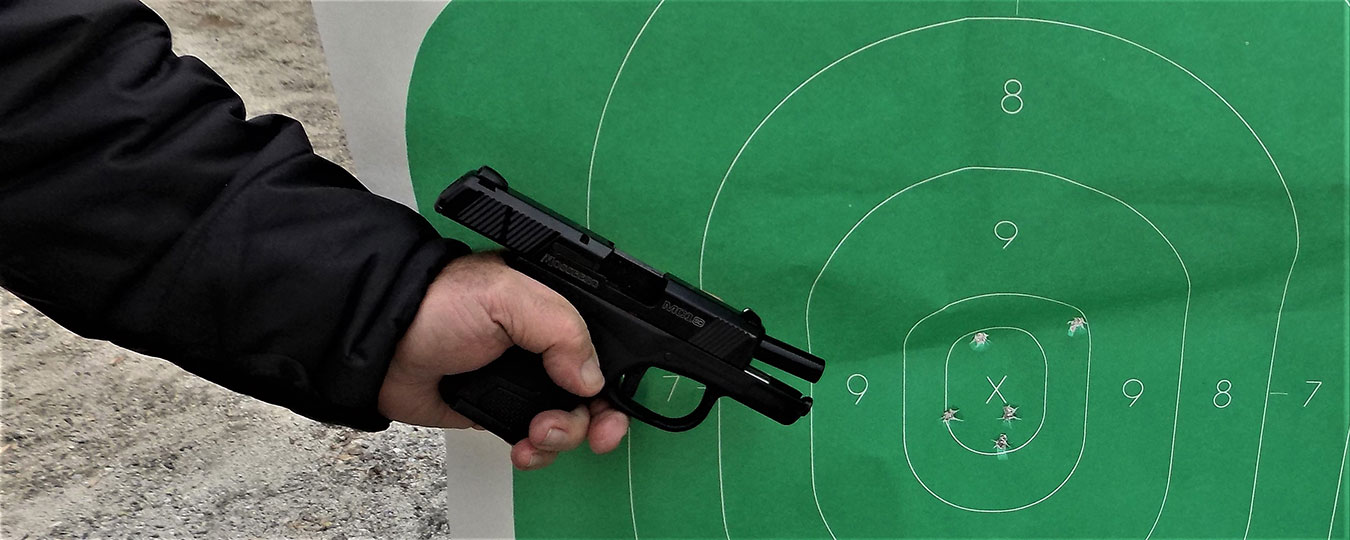 pistol with slide locked back in front of a green silhouette target with bullet holes