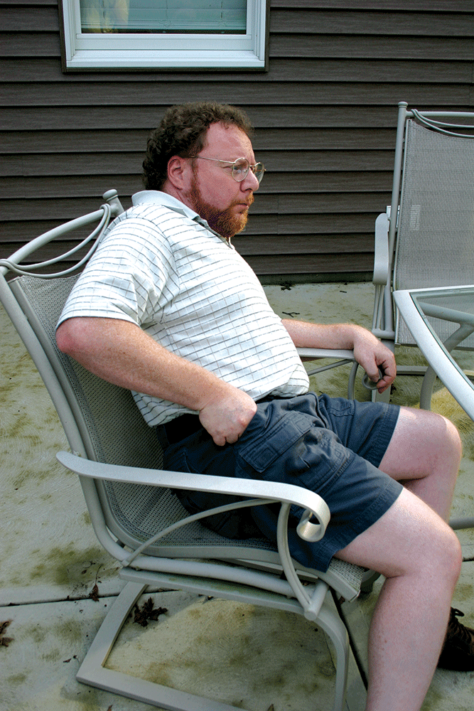 Man sitting in a lawn chair drawing a pistol from his pocket