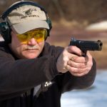 Man wearing safety glasses and hearing protection shooting a 1911 pistol with a two handed grip