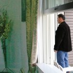 view of a man standing at the front door of a house from a bedroom window