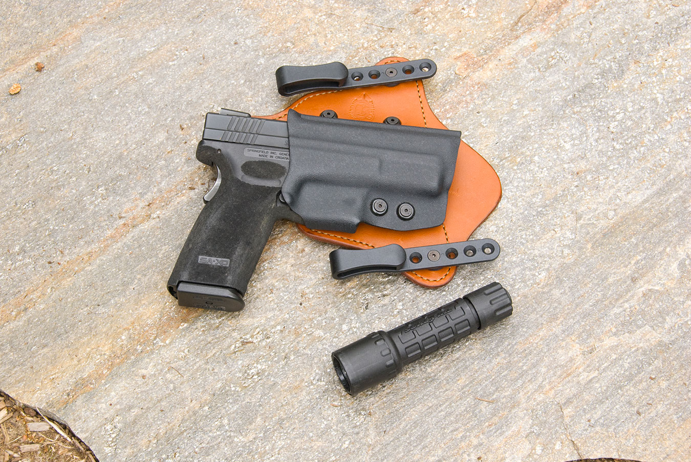 Springfield Armory XD45 in a leather and Kydex holster with a small black flashlight next to it