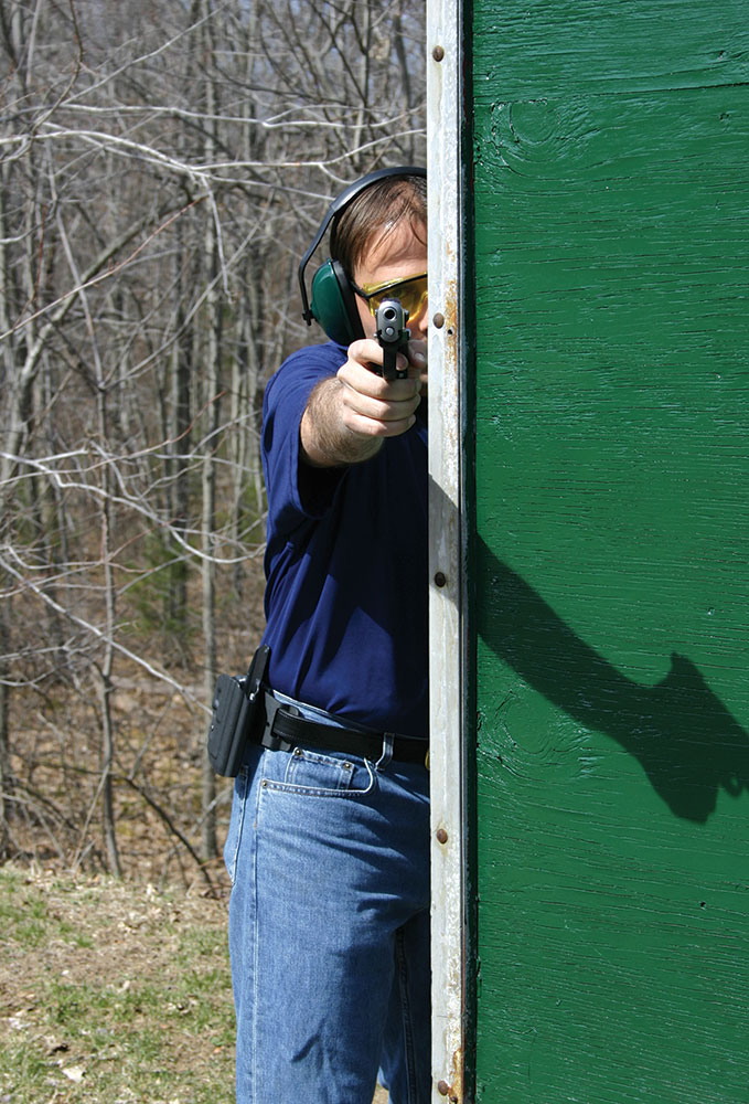 Man shooting a pistol with half of his body exposed and half behind cover