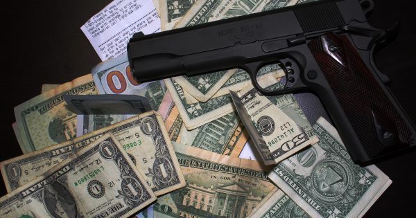 black handgun on top of a pile of paper money to protest gun control efforts of lobbyists
